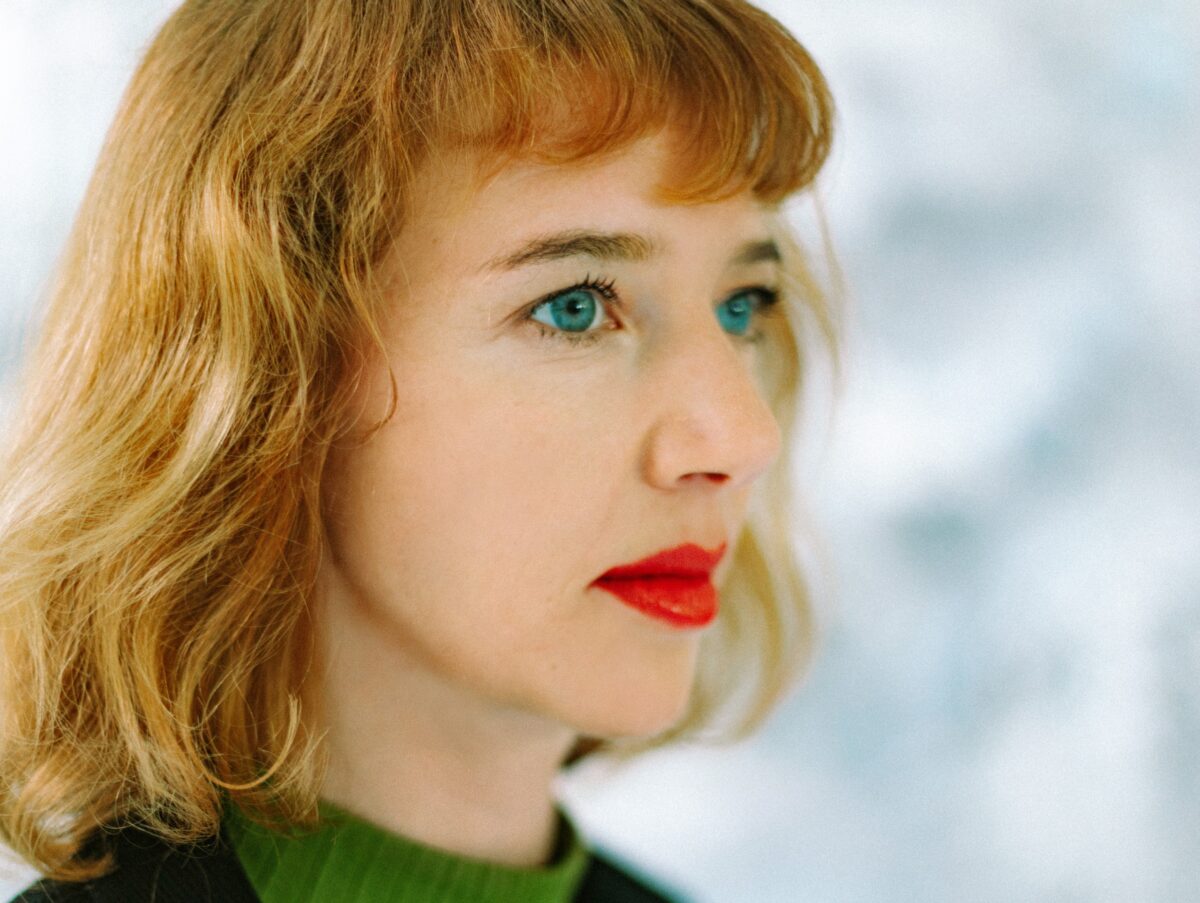 Gloria Benedikt schaut schräg in die Kamera und trägt kupferne Haare. Porträtbild.